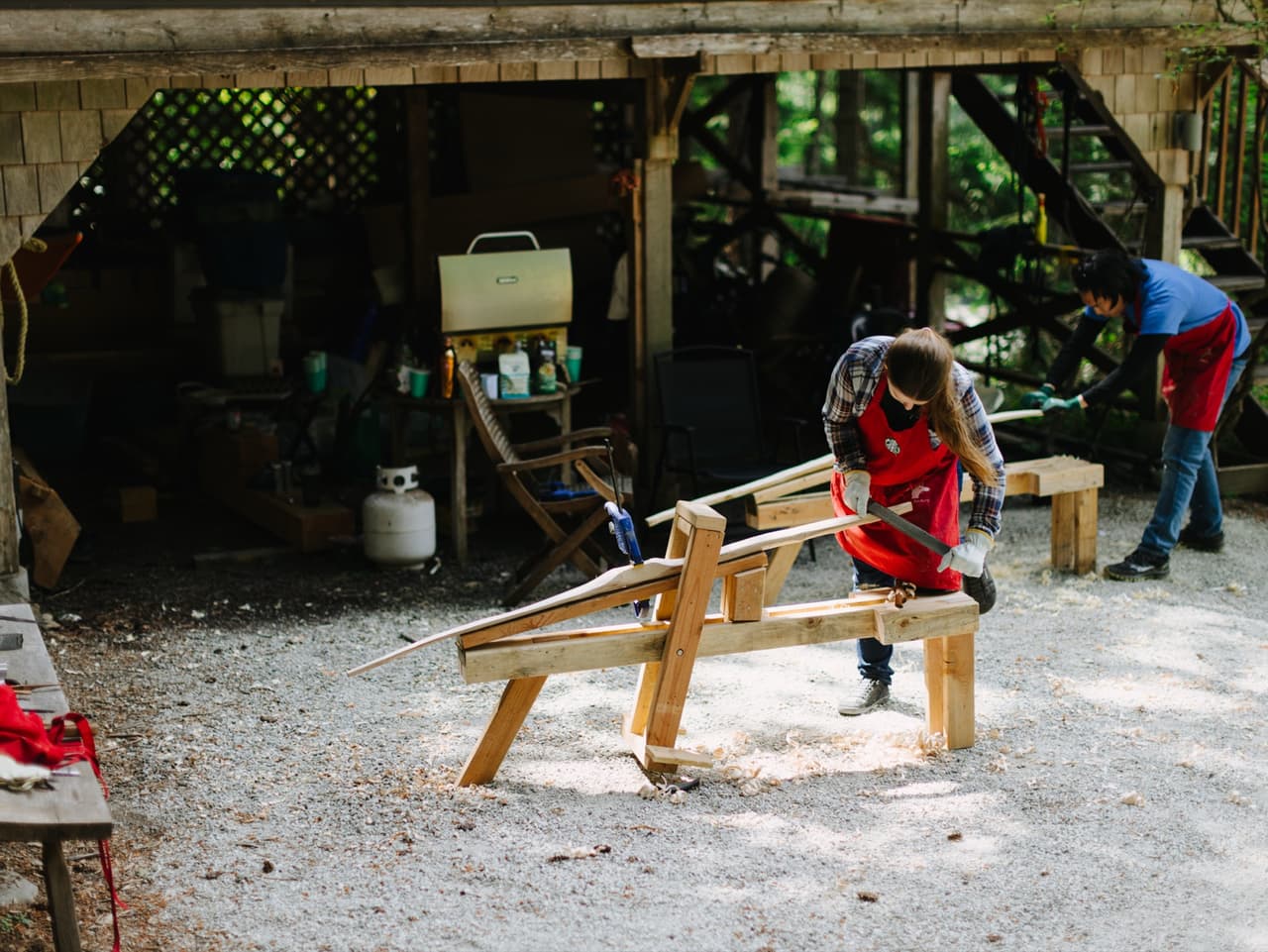 Workshop participants shaping bow staves on shaving horses outside the shop.