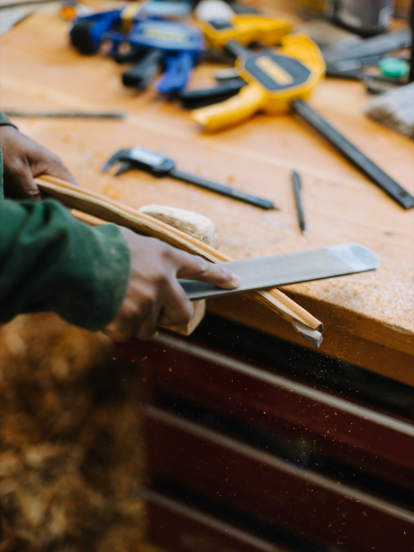 Hands working a rasp along the belly of a roughed-out bow limb.