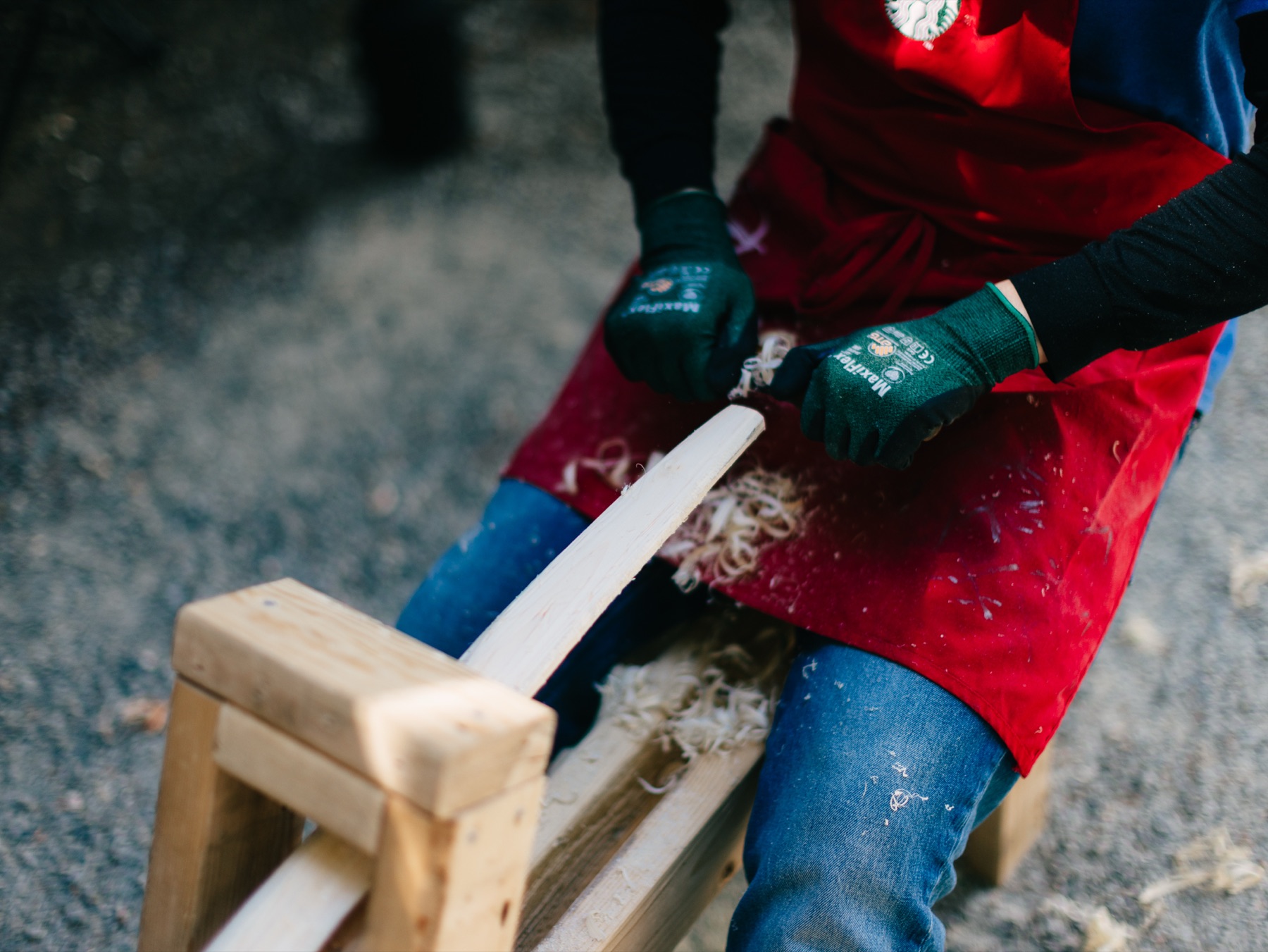 A young participant in gloves working a drawknife across a bow stave.