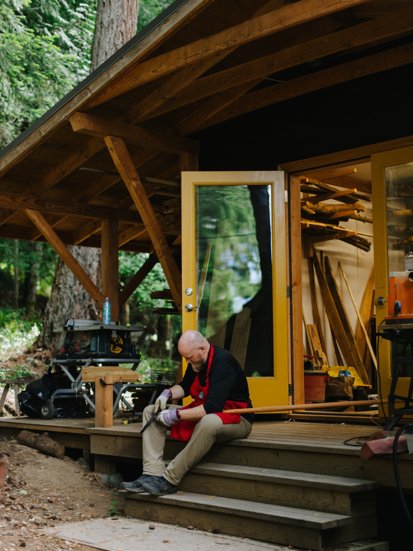 The open-sided workshop under cedar, tools racked along the back wall.
