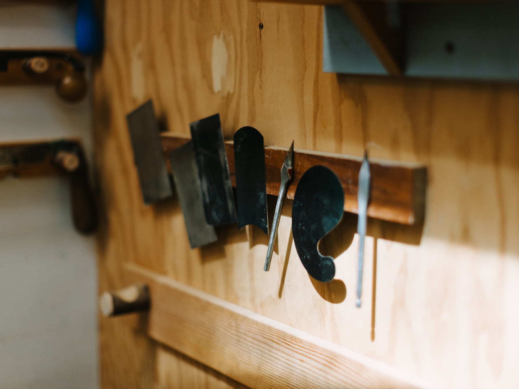Drawknives, rasps and scrapers hung in a row on the workshop wall.